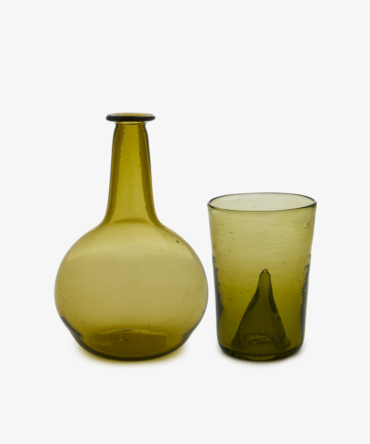 The Elodie Bedside Carafe and Glass Set, featuring a round-bottomed green glass carafe, sits next to its matching green hand-blown tumbler on a plain white background.
