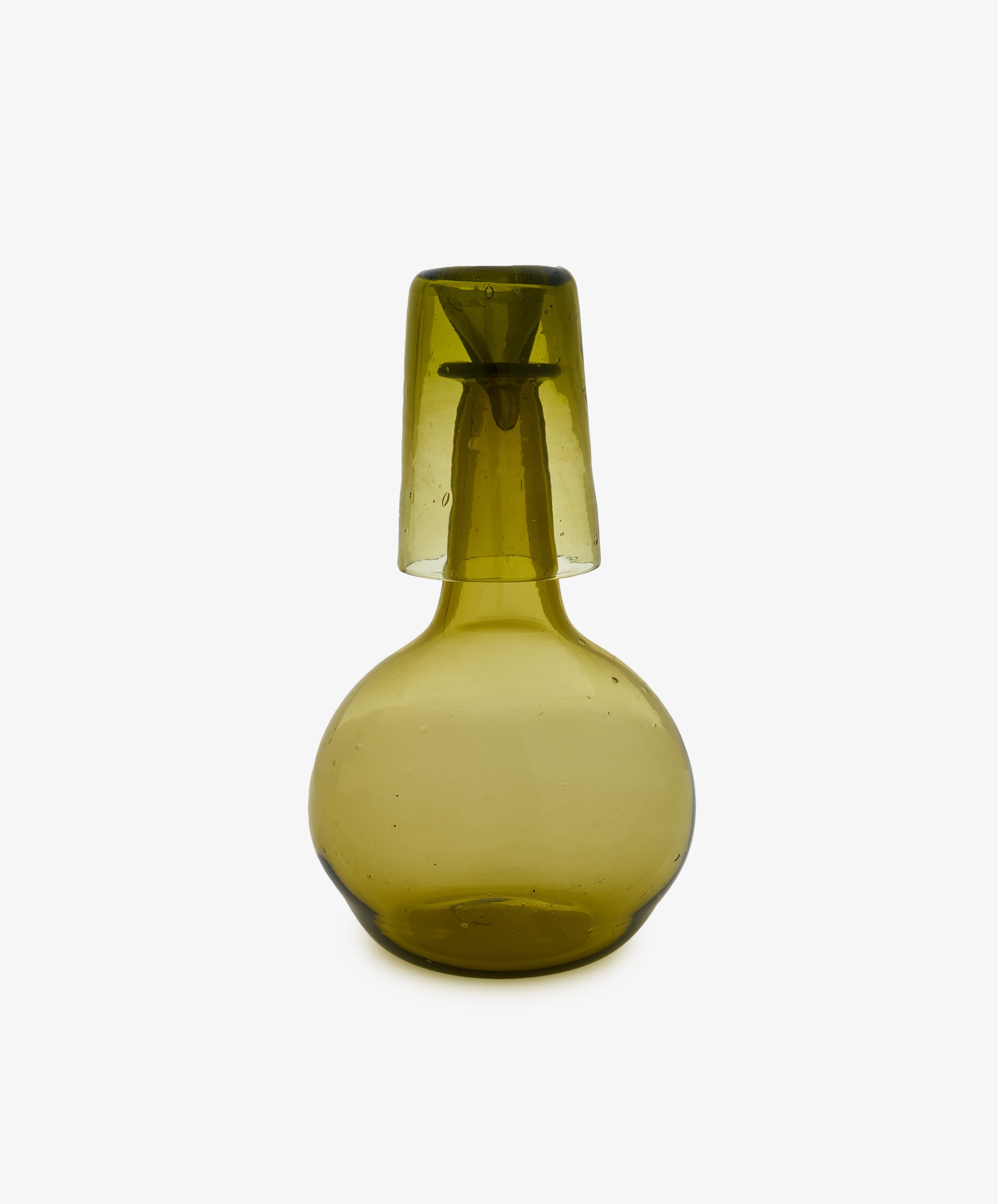 The Elodie Bedside Carafe and Glass Set features hand-blown green glass with a simple, rounded design and a slightly translucent finish; the matching cup inverts to rest atop the carafe, showcasing timeless elegance.