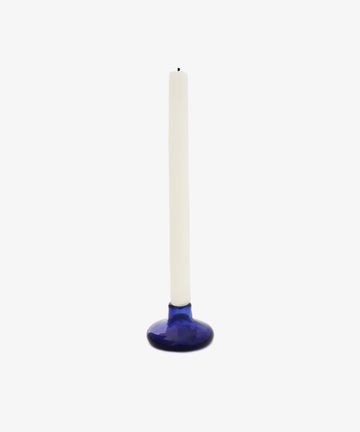 A white taper candle stands upright in the modern Lucien candleholder, made of cobalt glass, against a plain white background.