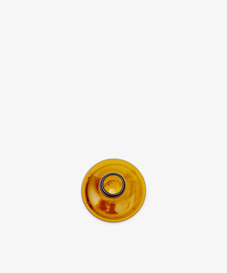 The Lucien candleholder, a round, amber glass piece handblown in Morocco from recycled glass, is viewed from above and placed near the lower center of a plain white background.