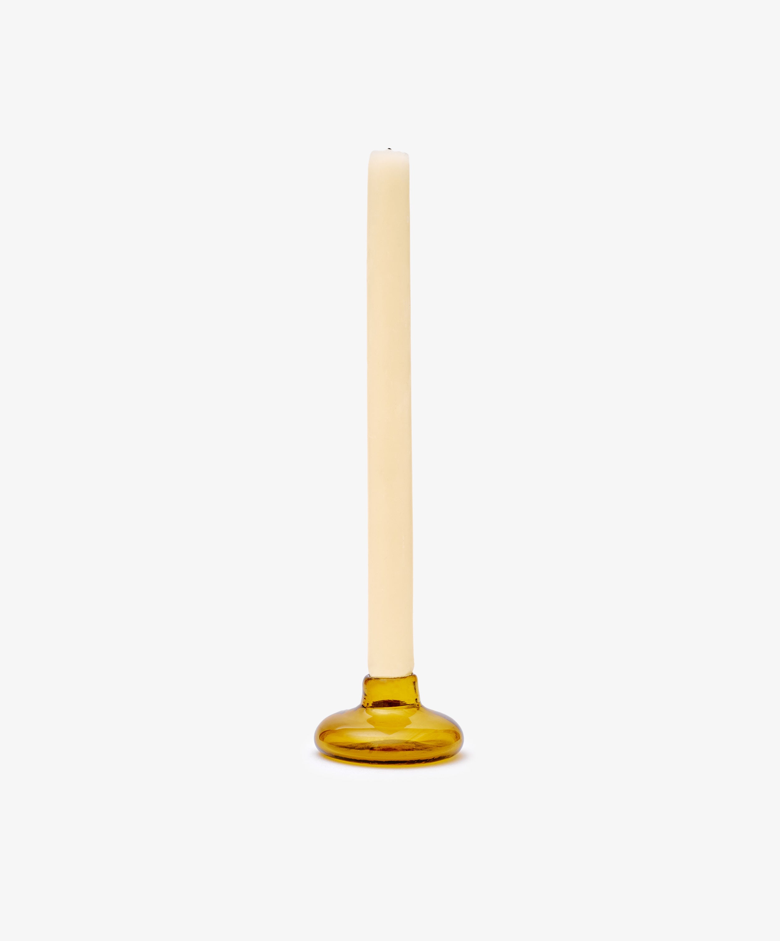 A single cream-colored taper candle sits in the Lucien candleholder, a round amber glass piece handblown in Morocco, set against a plain white background.