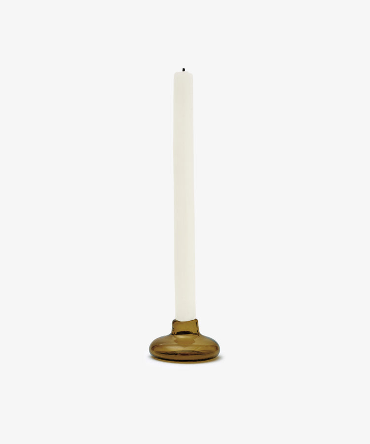 A white taper candle stands in the Lucien bubble candleholder, Small—a round, handblown brown glass holder from Morocco—set against a plain white background.