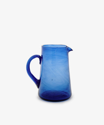 The Elodie Pitcher, a handblown glass piece in vibrant Moroccan blue with a handle and small spout, is shown against a plain white background.