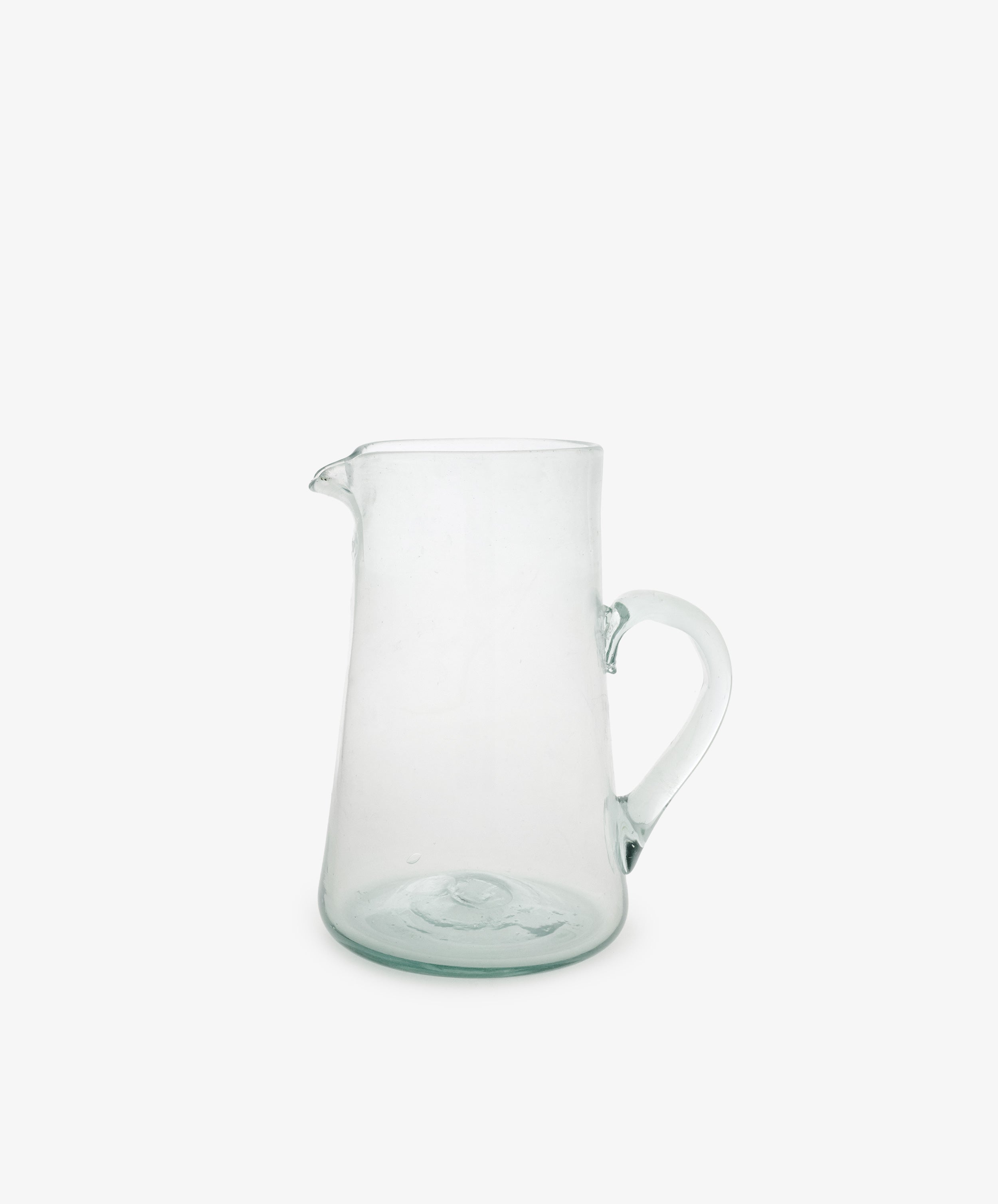 The Elodie Pitcher is a handblown clear glass pitcher with a handle and small spout, crafted in Damascus and shown against a plain white background.