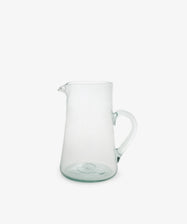 The Elodie Pitcher is a handblown clear glass pitcher with a handle and small spout, crafted in Damascus and shown against a plain white background.