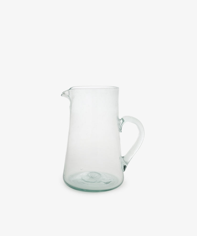 The Elodie Pitcher is a handblown clear glass pitcher with a handle and small spout, crafted in Damascus and shown against a plain white background.