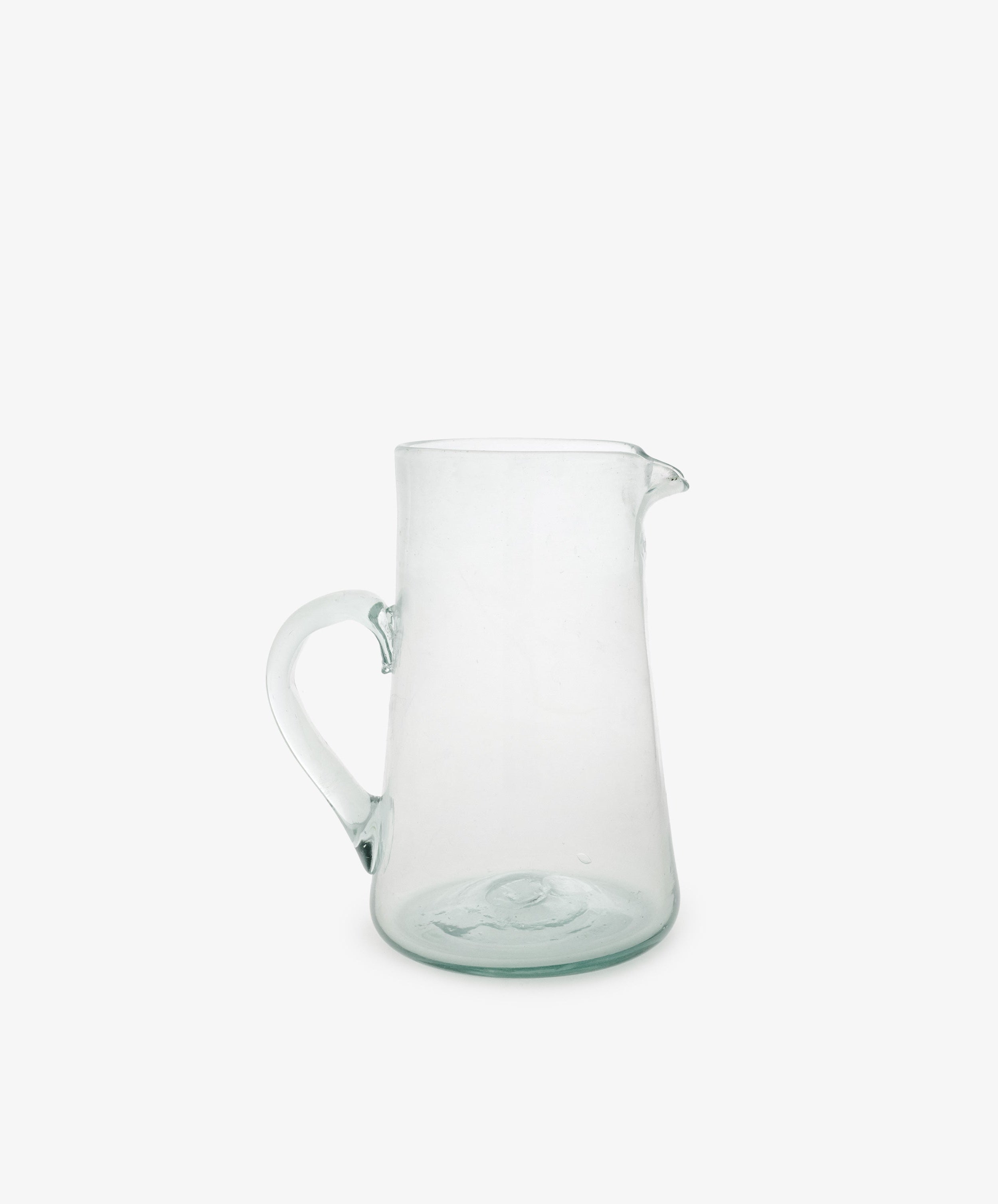 The Elodie Pitcher is a handblown clear glass pitcher with a handle and small spout, crafted in Damascus and shown against a plain white background.