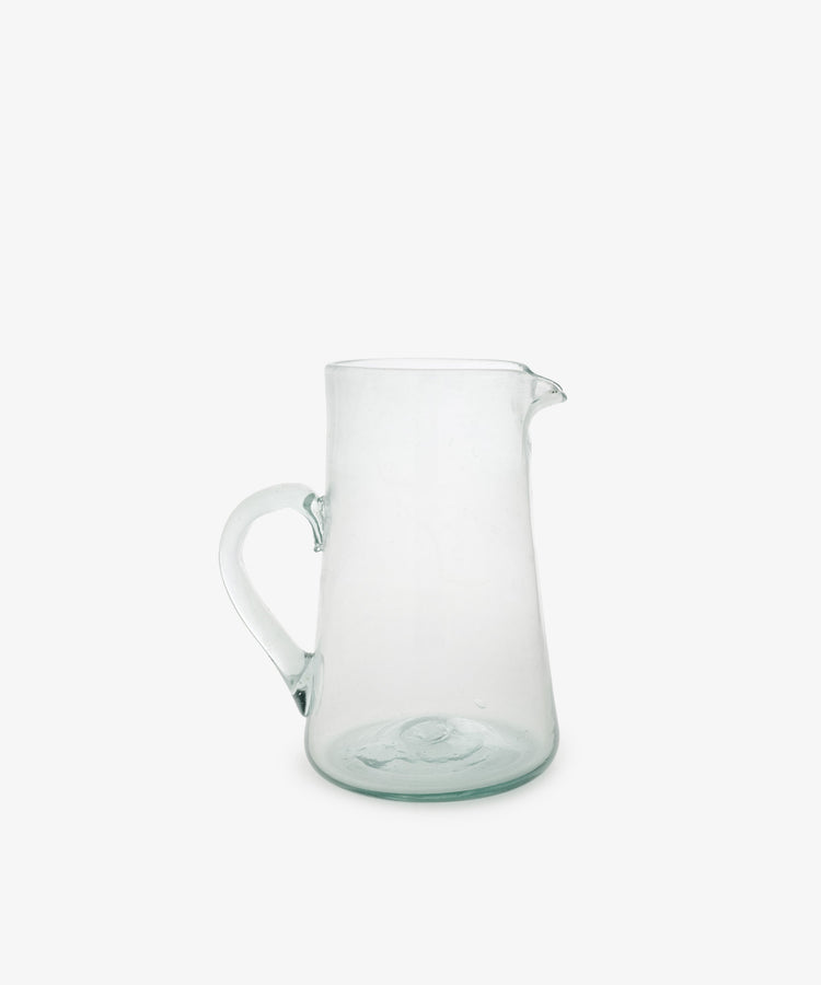 The Elodie Pitcher is a handblown clear glass pitcher with a handle and small spout, crafted in Damascus and shown against a plain white background.