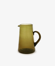 The Elodie Pitcher is a handblown, translucent olive-green glass pitcher from Damascus, featuring a handle and spout, shown against a white background.