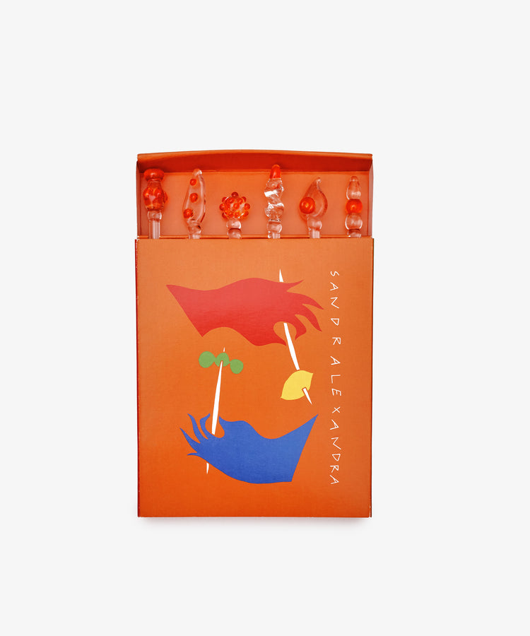 The Festa Cocktail and Nibble Sticks set includes six uniquely shaped decorative picks, presented in an orange box with abstract face artwork and 