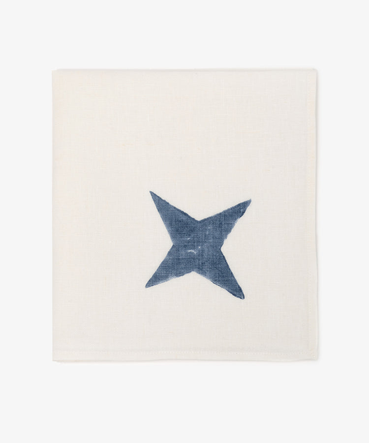 The Nova Napkin, Set of 6, features square ivory linen napkins with a hand block-printed blue X-shaped design at the center—perfect for adding a unique touch to your table settings.