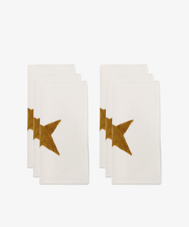 Six Nova linen napkins, each hand block-printed with a partial gold star design on one side, are arranged in two rows against a plain white background.