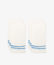 Six Onda napkins, white linen with two blue wave-like stripes near one edge, arranged in two stacks against a plain white background.