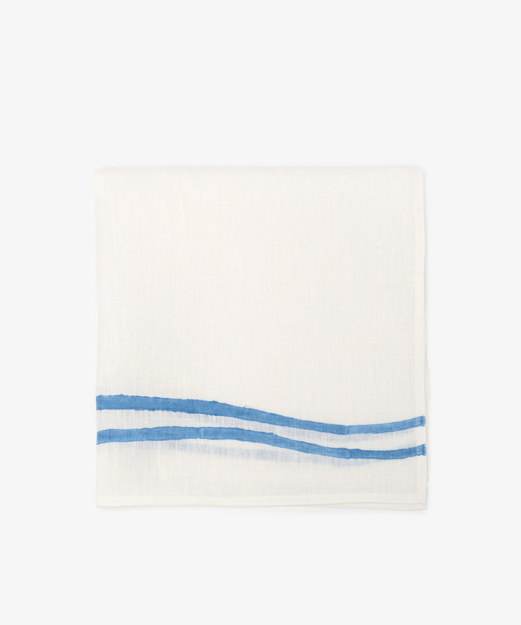 A set of 6 Onda Napkins, each made of folded white linen and hand block-printed with two parallel blue wave-like stripes along one edge, displayed against a plain background.