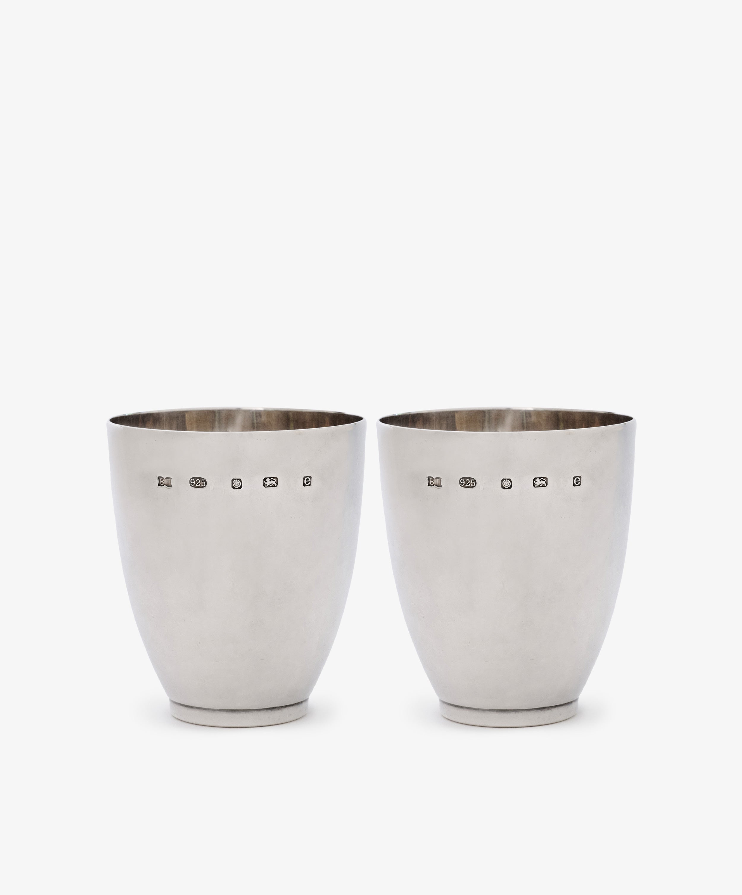 A Vintage Pair of Silver Beakers, hallmarked Sheffield 2004, polished to a bright finish, are displayed side by side on a white background—elegant contemporary camp cups with timeless appeal.