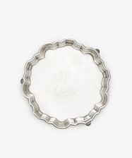 The Vintage English Salver is an 18th-century silver round tray with scalloped edges, three small feet, and a central engraved decorative pattern.