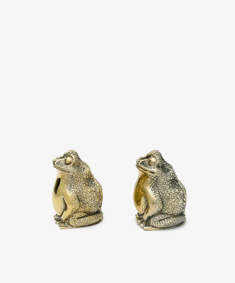 A vintage pair of Tiffany frog salt and pepper shakers—one gold, one with a silver finish—are displayed side by side on a plain white background.
