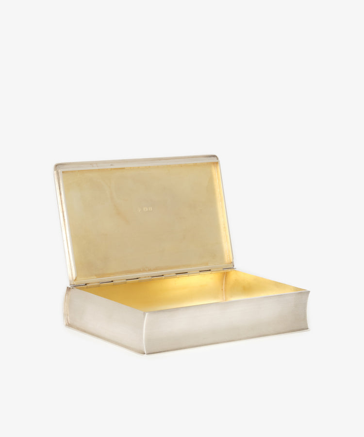 The Vintage Cigarette Box Book features a rectangular sterling silver exterior styled like a closed book, a hinged lid, and a gold-colored interior—making it a unique collectible inspired by the timeless charm of Robert Burns poetry.