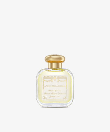 A clear glass bottle of Acqua Della Regina Eau de Cologne, a historic scent, features a gold cap and cream label with gold lettering and decorative accents.
