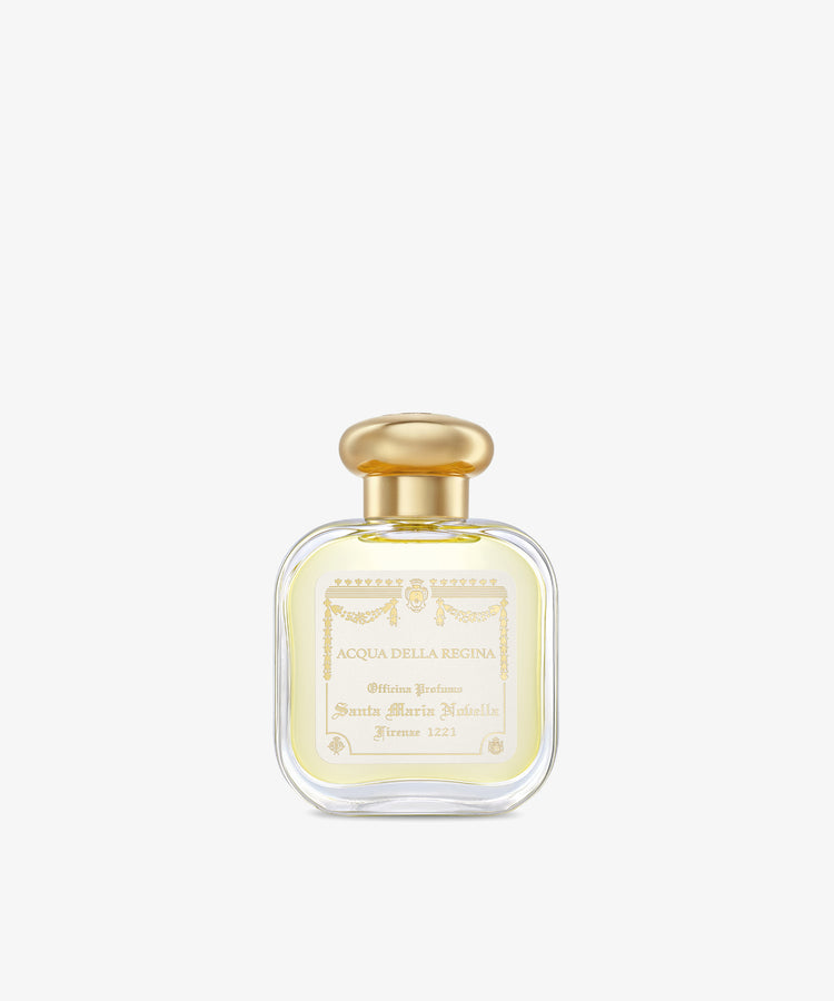 A clear glass bottle of Acqua Della Regina Eau de Cologne, a historic scent, features a gold cap and cream label with gold lettering and decorative accents.