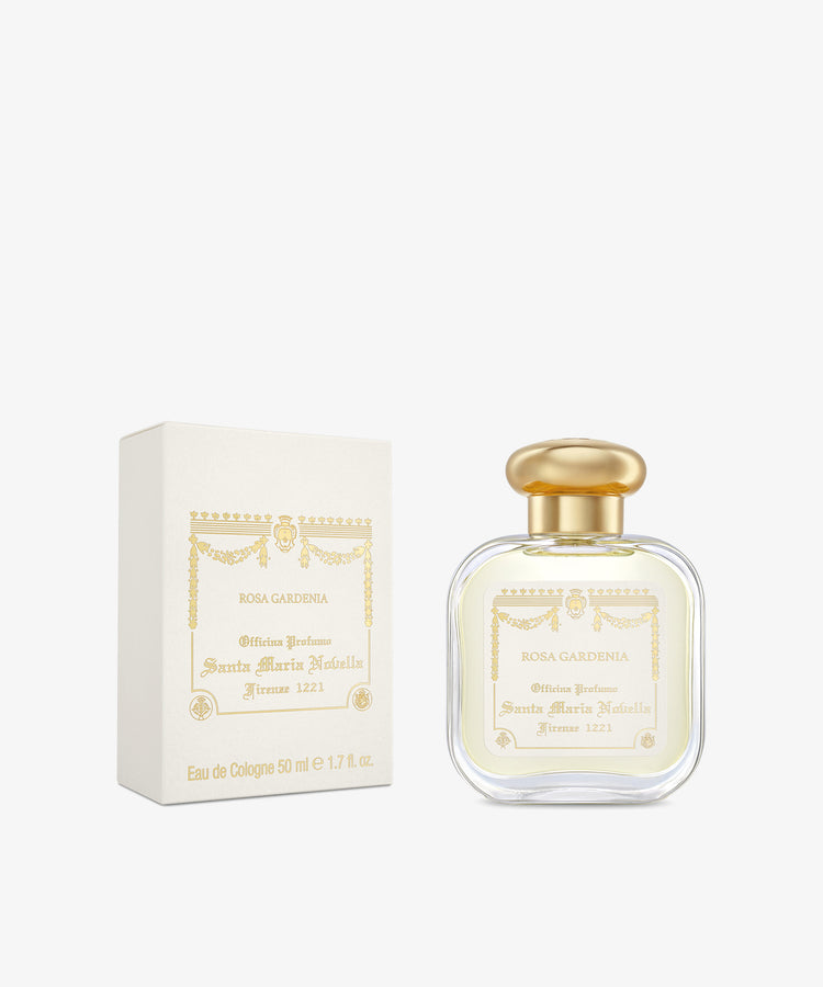 A bottle of Rosa Gardenia Eau de cologne with a gold cap is shown beside its cream-colored, gold-detailed box, highlighting this elegant floral fragrance from Santa Maria Novella.