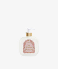 A white pump bottle with a gold dispenser, labeled Rosa Gardenia Fluid Body Cream on a pink and gold label, sits against a plain white background, offering a nourishing cream with a floral fragrance.