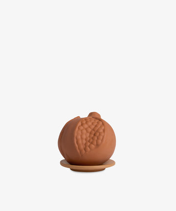 The Pomegranate in Scented Terracotta is a small, round terracotta object with a textured leaf design, displayed on a matching circular base against a plain white background.