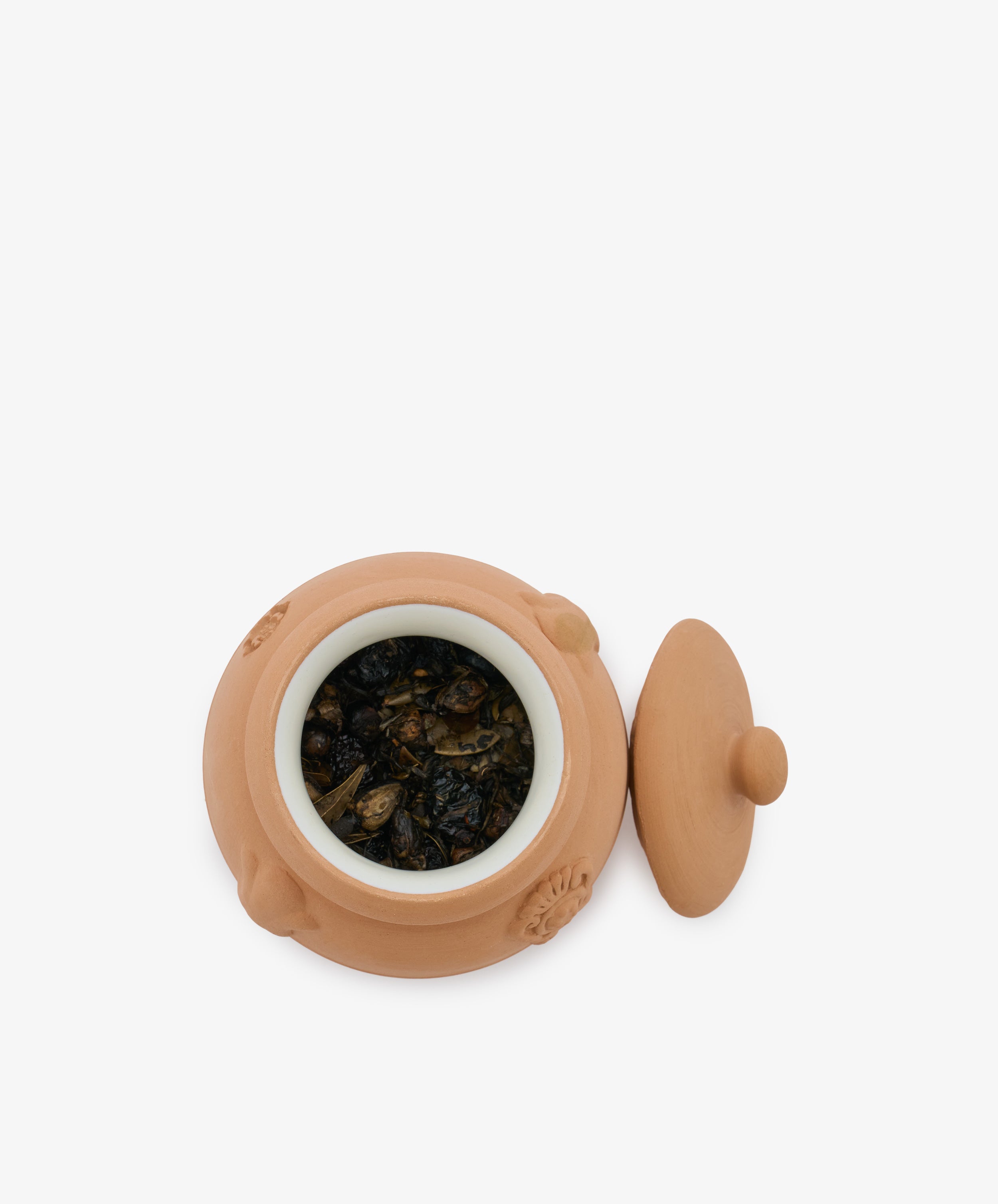 A small terracotta Pot Pourri jar with a white inner lining, filled with a traditional herbal blend, sits with its lid placed beside it on a white background.