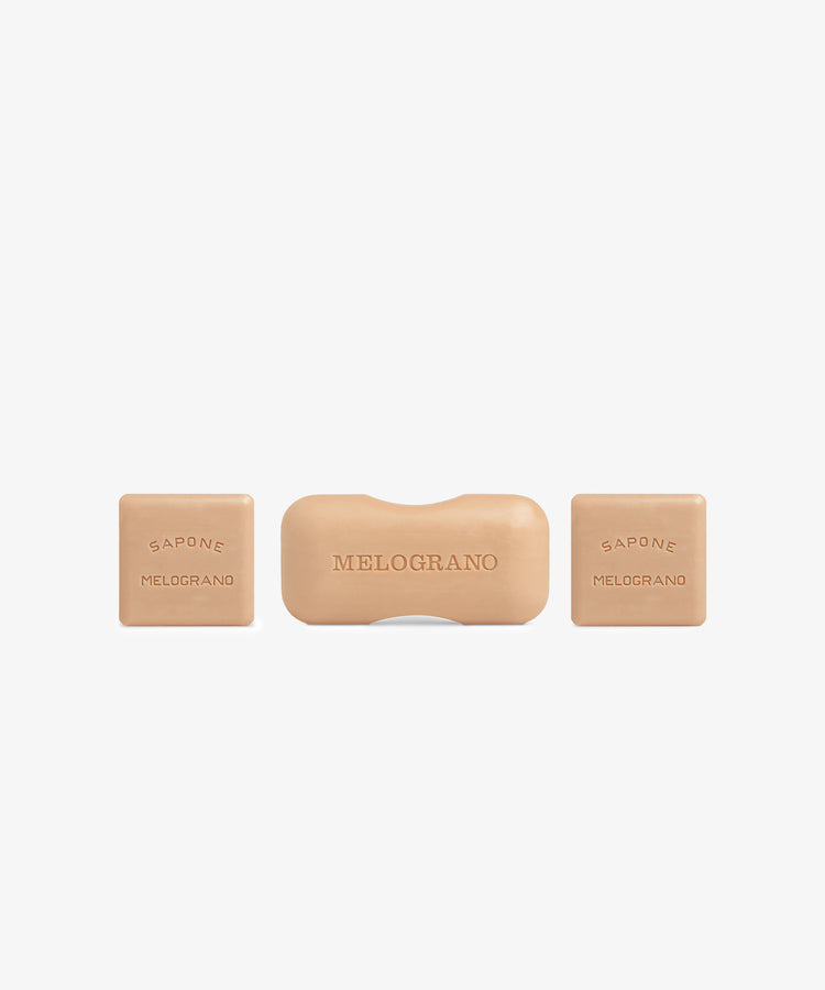 The Melograno Soap Set includes three beige bars from Santa Maria Novella on a white background: a rectangular center bar labeled “MELOGRANO” and two square side bars reading “SAPONE MELOGRANO.”.