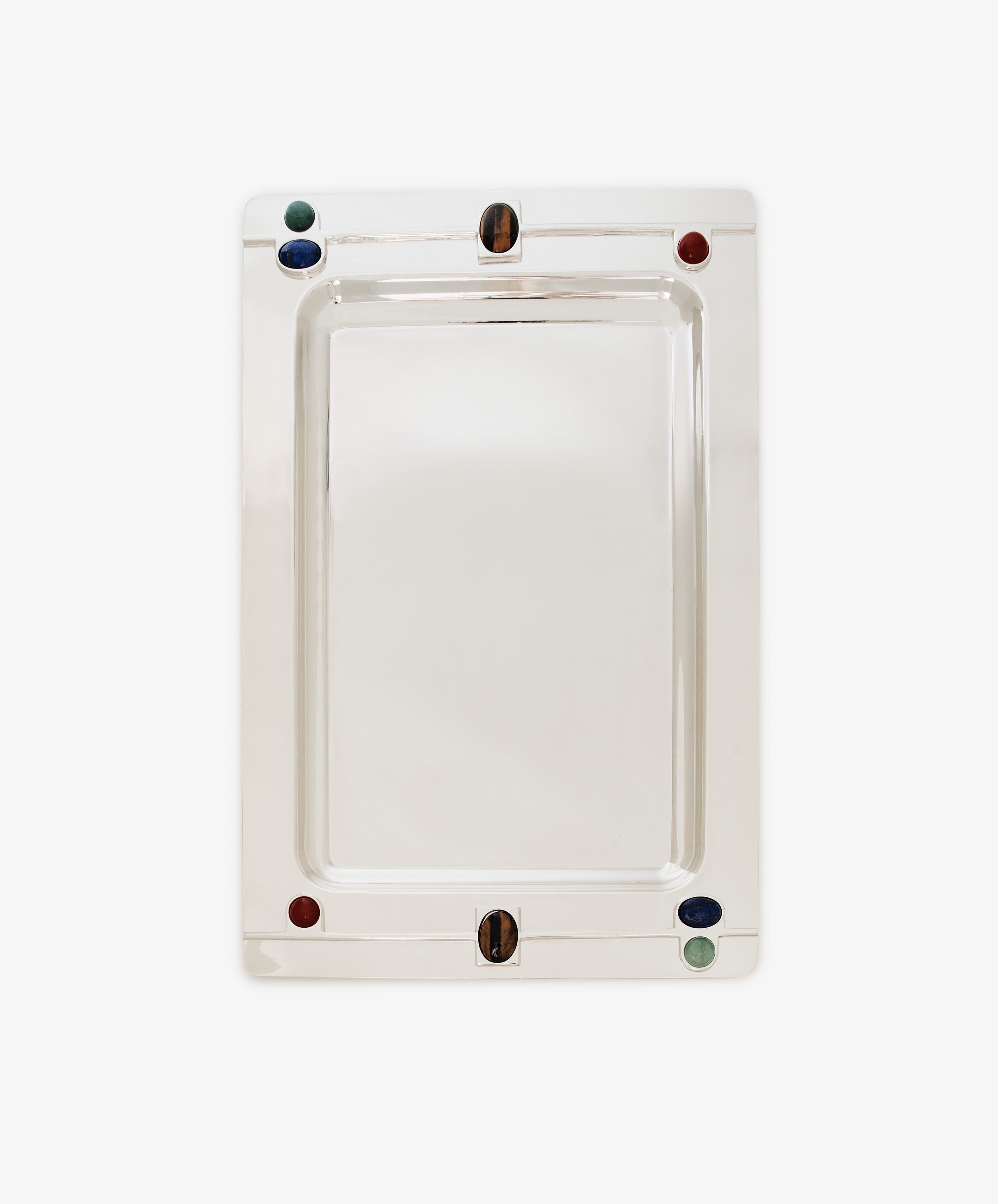 The Verola Rectangle Tray is a polished silver tray with rounded corners, adorned with four colored accents—two red, one green, and one blue stones or glass pieces—set near the edges. This decorative tray is presented on a white background.