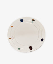 The Verola Round Tray, featuring a smooth silver surface and several colorful oval stones embedded around its rim to resemble a colored stone ring, is displayed on a white background.