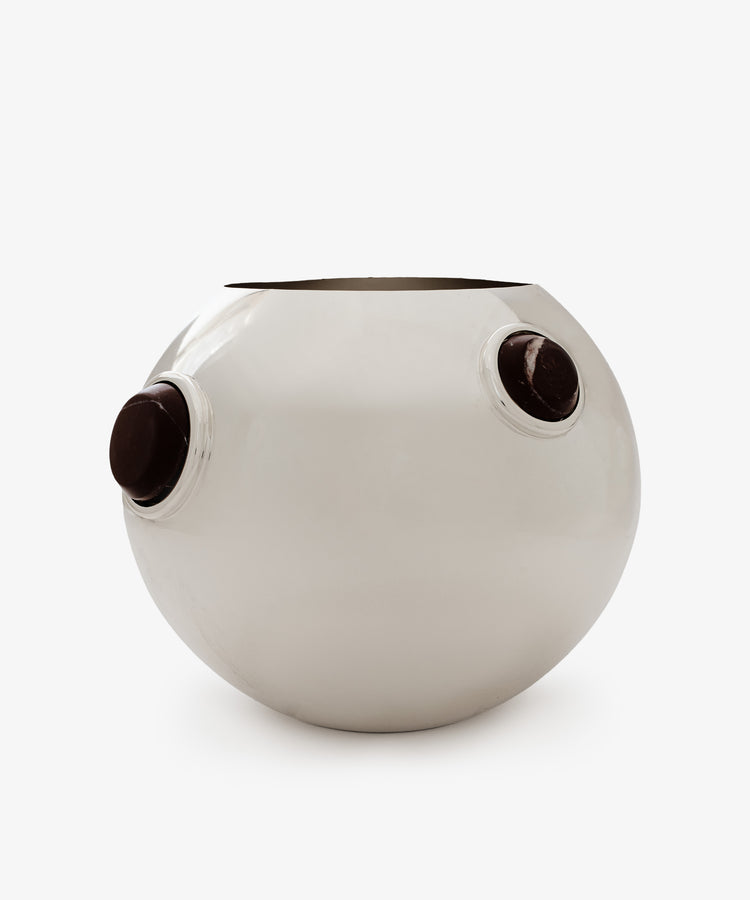 The Paros Round Vase is a silver metallic piece featuring a mirror-polished sphere finish and two circular dark brown knobs on opposite sides, shown against a plain white background.