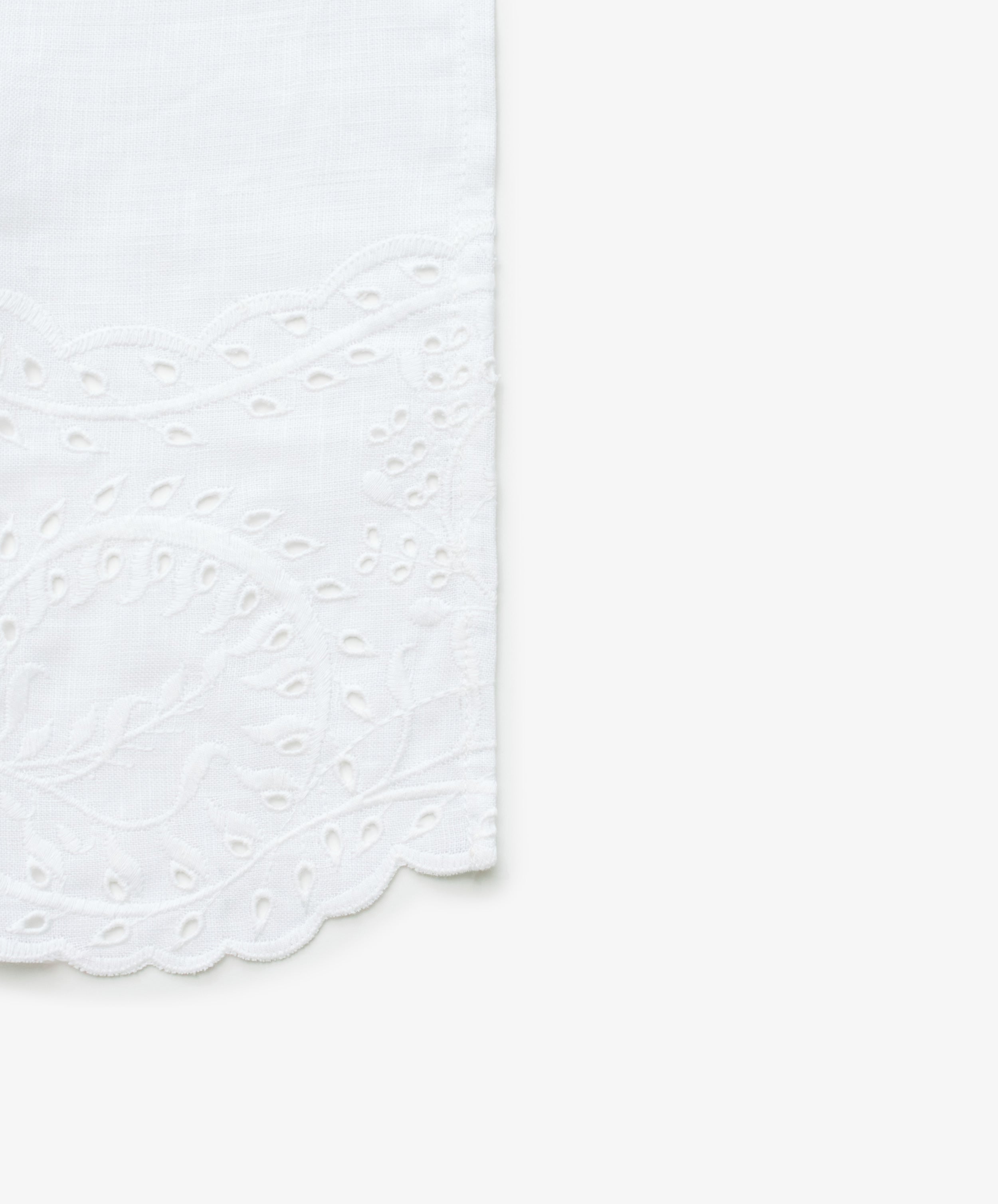 Close up view of white linen napkin with embroidered edges.