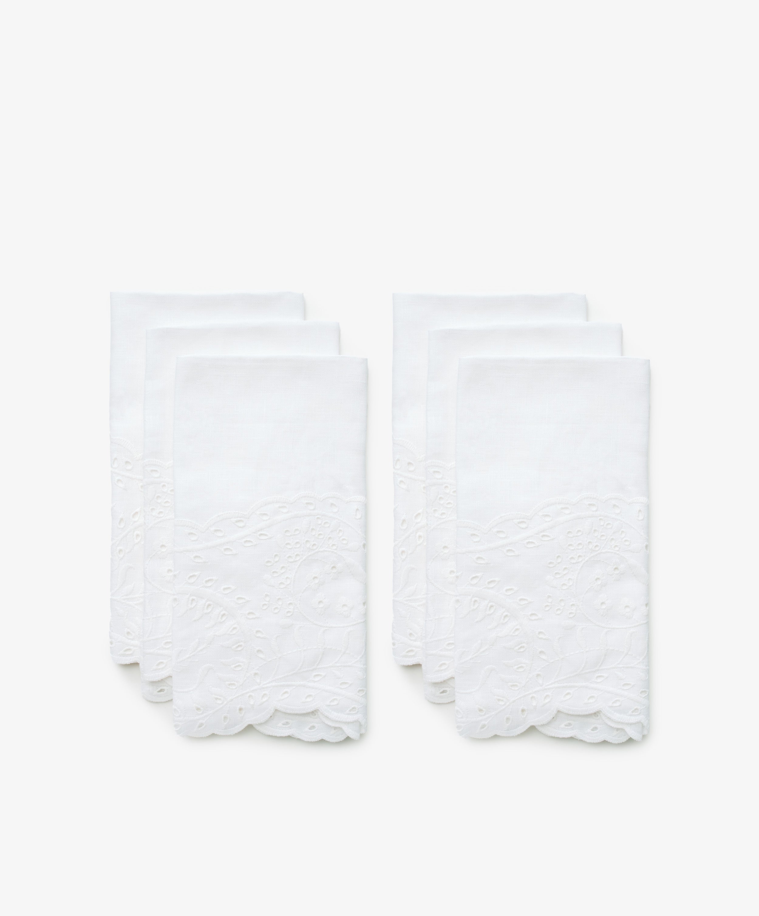 A set of six white linen napkins with eyelet embroidery. Front view.