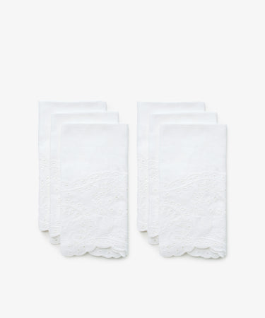 A set of six white linen napkins with eyelet embroidery. Front view.