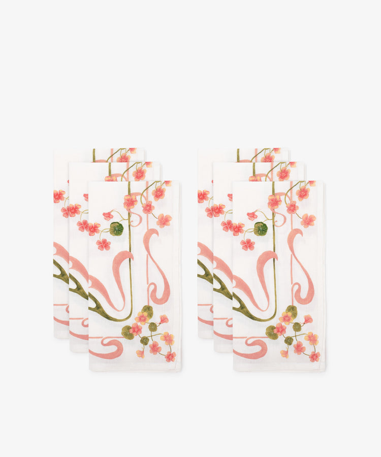 The Capucines Linen Napkin set includes six white napkins with a pink floral and vine Art Nouveau design, displayed in two overlapping stacks on a white background.