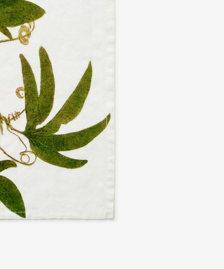 Tisane Herb Napkin. Green vine pattern on white linen. Close up of corner.