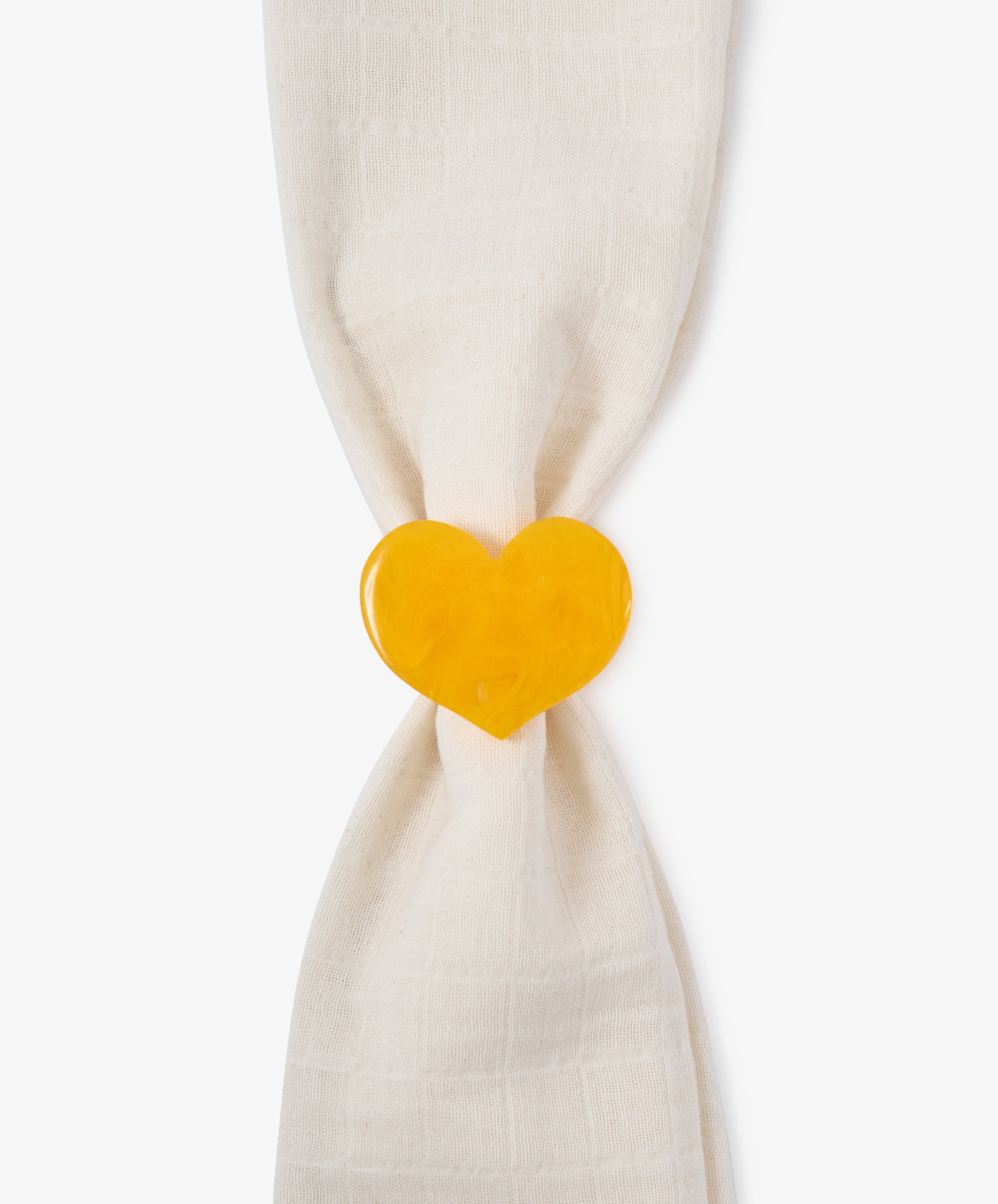 A cream-colored cloth napkin is gathered by the Heart Resin Napkin Ring, its sculptural, yellow heart form elegantly expressing love against a white background.