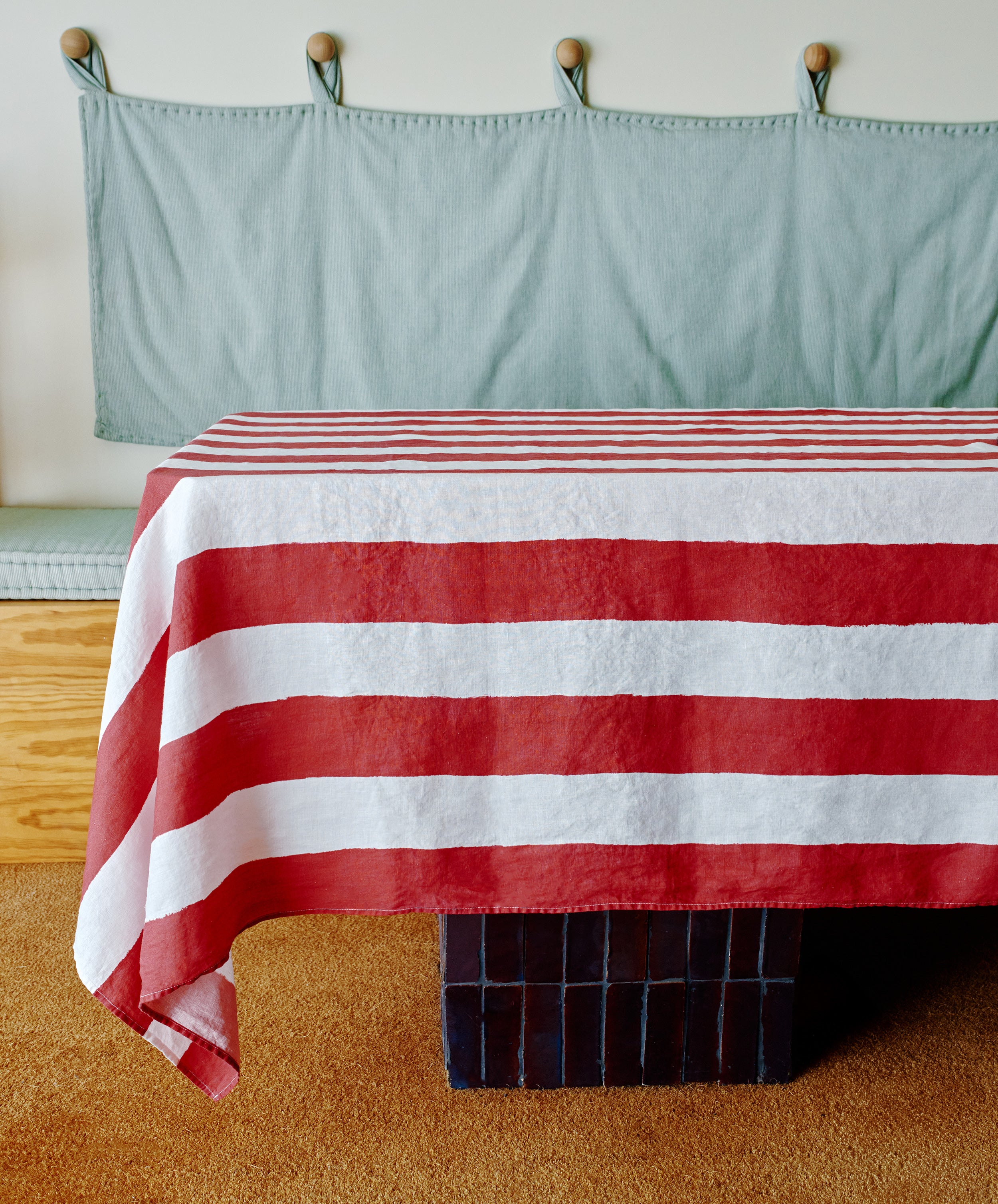 A Striped Tablecloth in festive red and white covers a table on a carpeted floor, with a cushioned bench and wall hooks visible in the background.