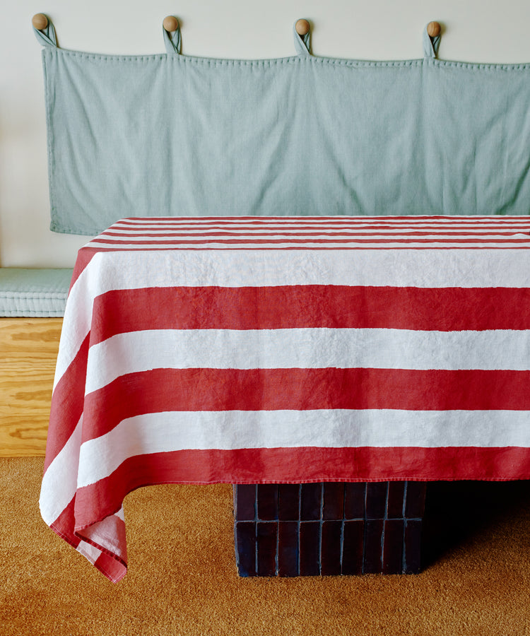 A Striped Tablecloth in festive red and white covers a table on a carpeted floor, with a cushioned bench and wall hooks visible in the background.