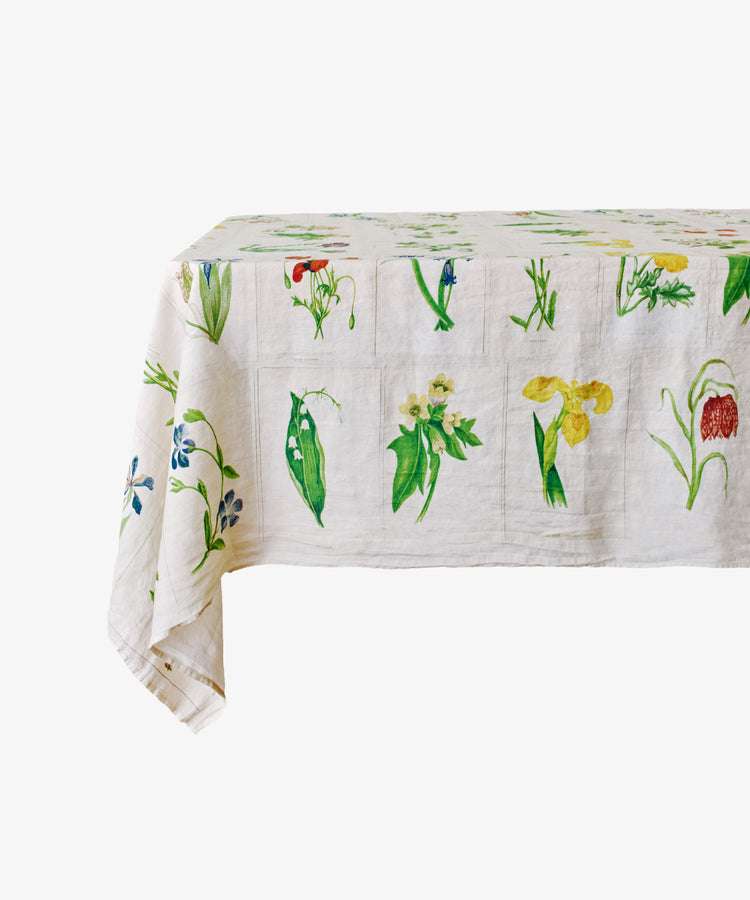 A rectangular table covered with the John Derian Botanical Tiles Tablecloth, featuring a vibrant botanical design with colorful floral and leaf illustrations.