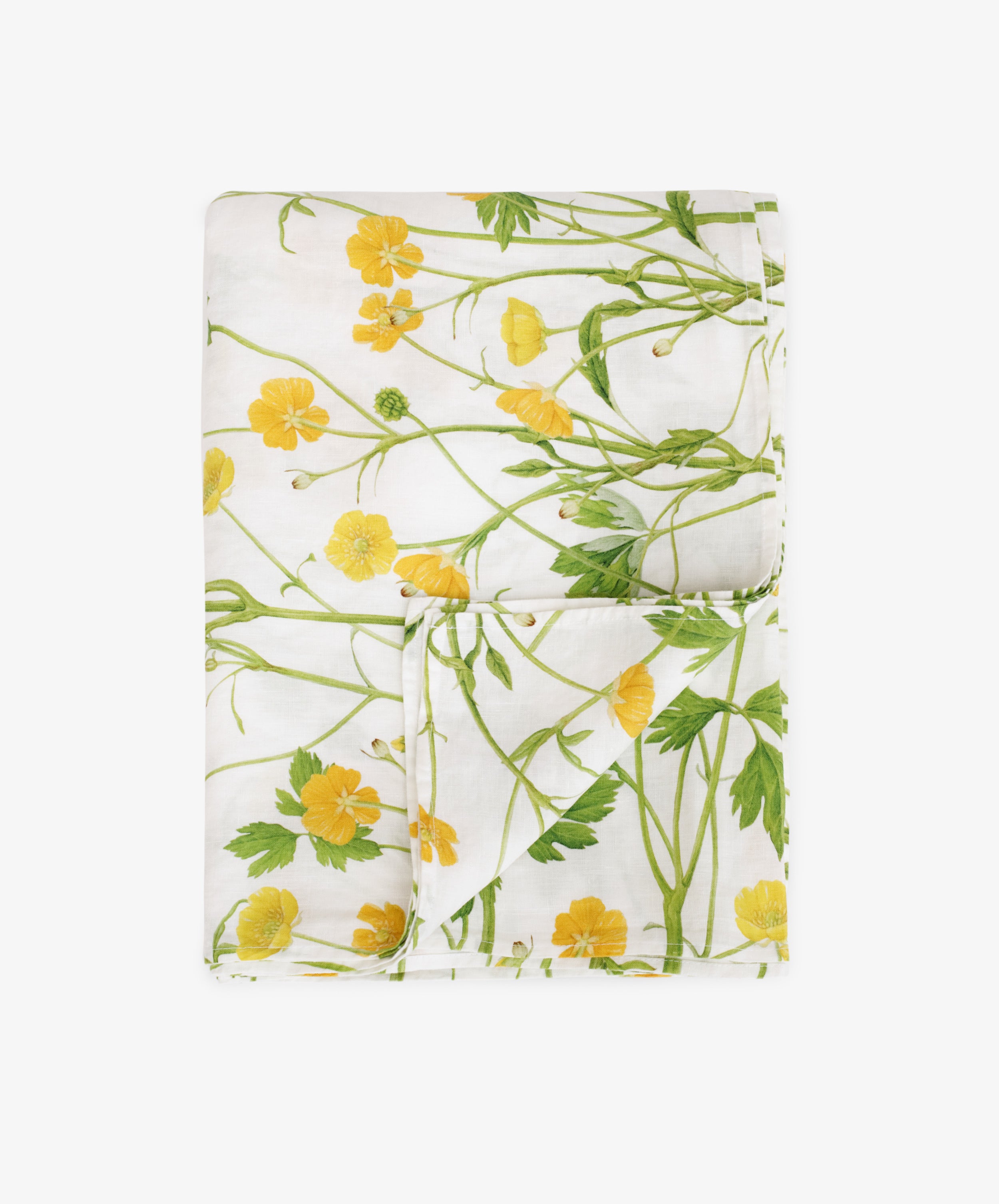 The Buttercup Linen Tablecloth features a folded white linen fabric with yellow buttercup floral and green leafy print, displayed on a plain white background—ideal for garden table decor.