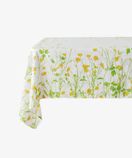 The Buttercup Linen Tablecloth, featuring green stems and yellow flowers on white linen, is draped over a rectangular table.