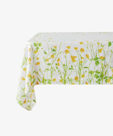 The Buttercup Linen Tablecloth, featuring green stems and yellow flowers on white linen, is draped over a rectangular table.