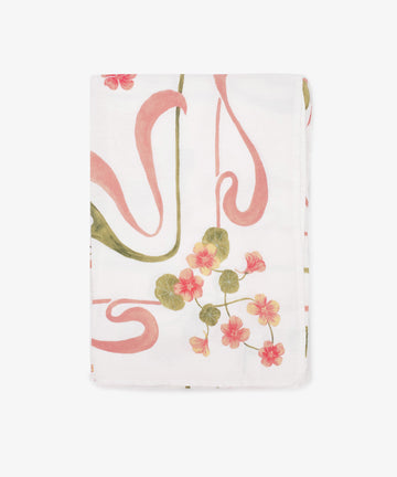 The Capucines Tablecloth is a folded white garden tablecloth with a botanical print of pink and yellow flowers and green leaves.