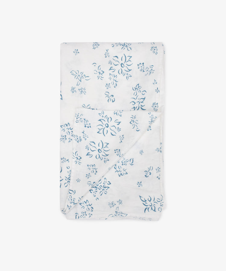 The Falling Flower Linen Tablecloth by Summerill & Bishop is shown folded on a white background, featuring a white linen fabric with a blue hand-drawn flower pattern.