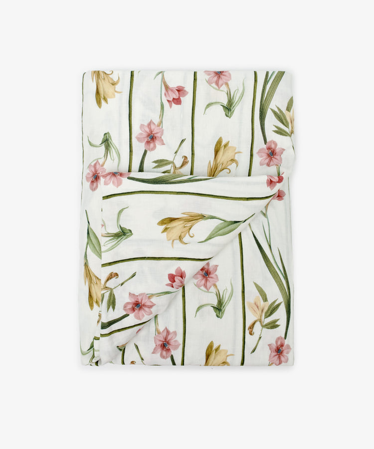 The Gladioli Tablecloth features a folded white fabric with pink and yellow gladioli flowers and green stems on a plain background—perfect for vibrant table décor.