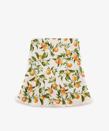 The L’Orangerie Round Linen Tablecloth features a vibrant orange fruit and green leaf pattern, reminiscent of classical French garden motifs, displayed against a crisp white background.
