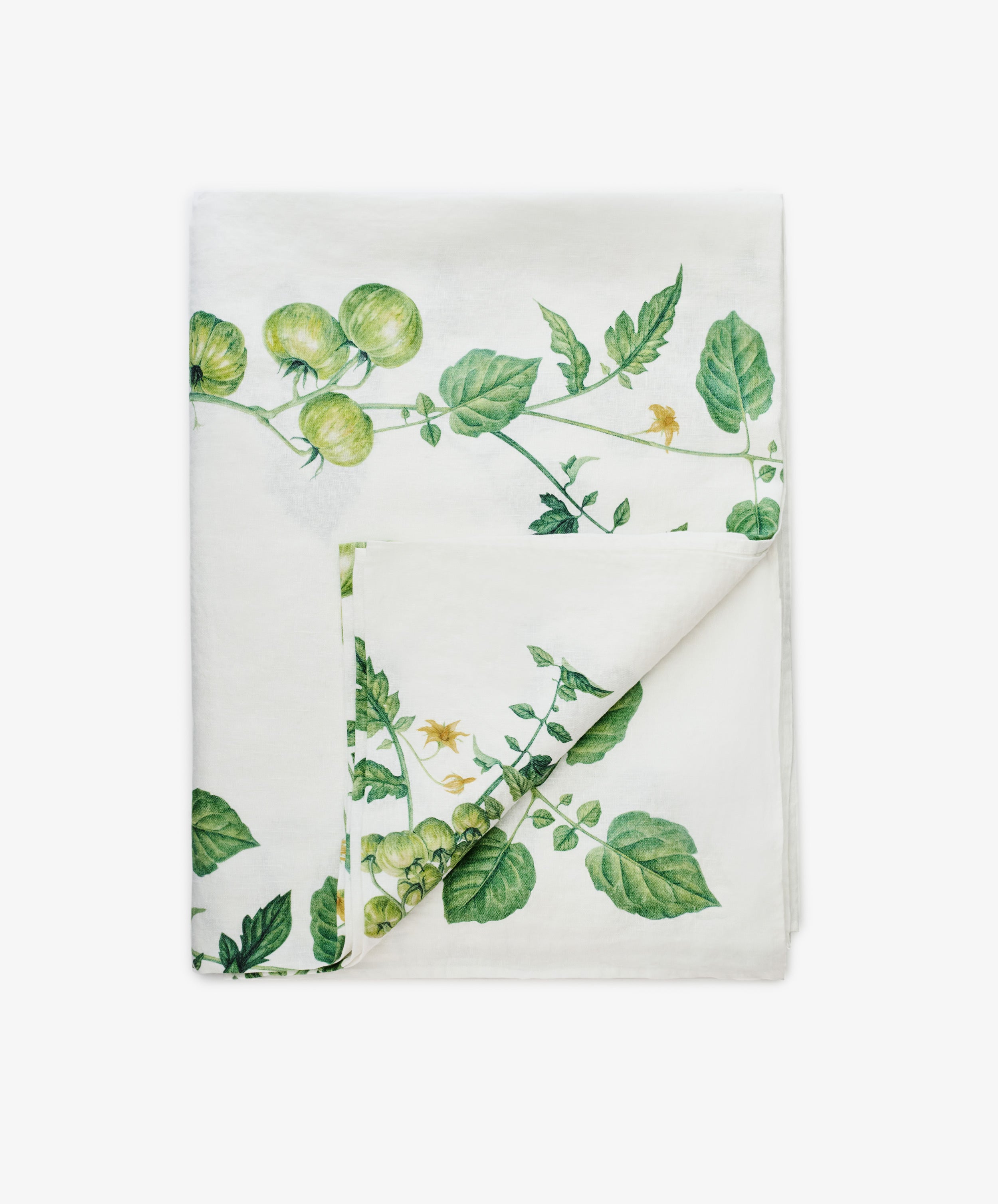 The Tomate Verte Linen Tablecloth from Summerill & Bishop features a folded white linen design with a green vine and tomato botanical print on one side.