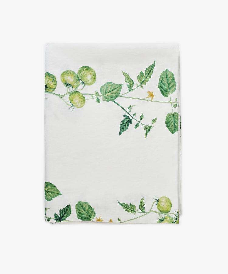 A white cloth napkin by Summerill & Bishop, featuring a Tomate Verte green tomato vine and leaf pattern along two edges, pairs beautifully with the matching Tomate Verte Linen Tablecloth.
